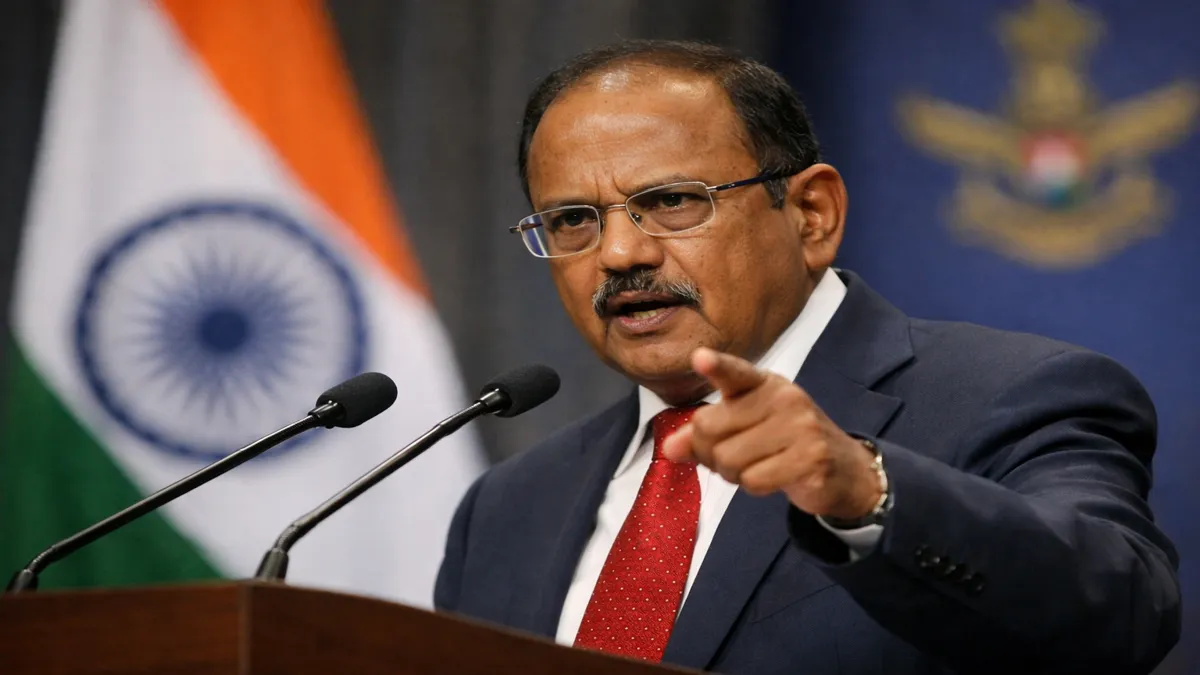 Ajit Doval delivering a speech at a podium, pointing forward while addressing an audience, with the Indian flag in the background.
